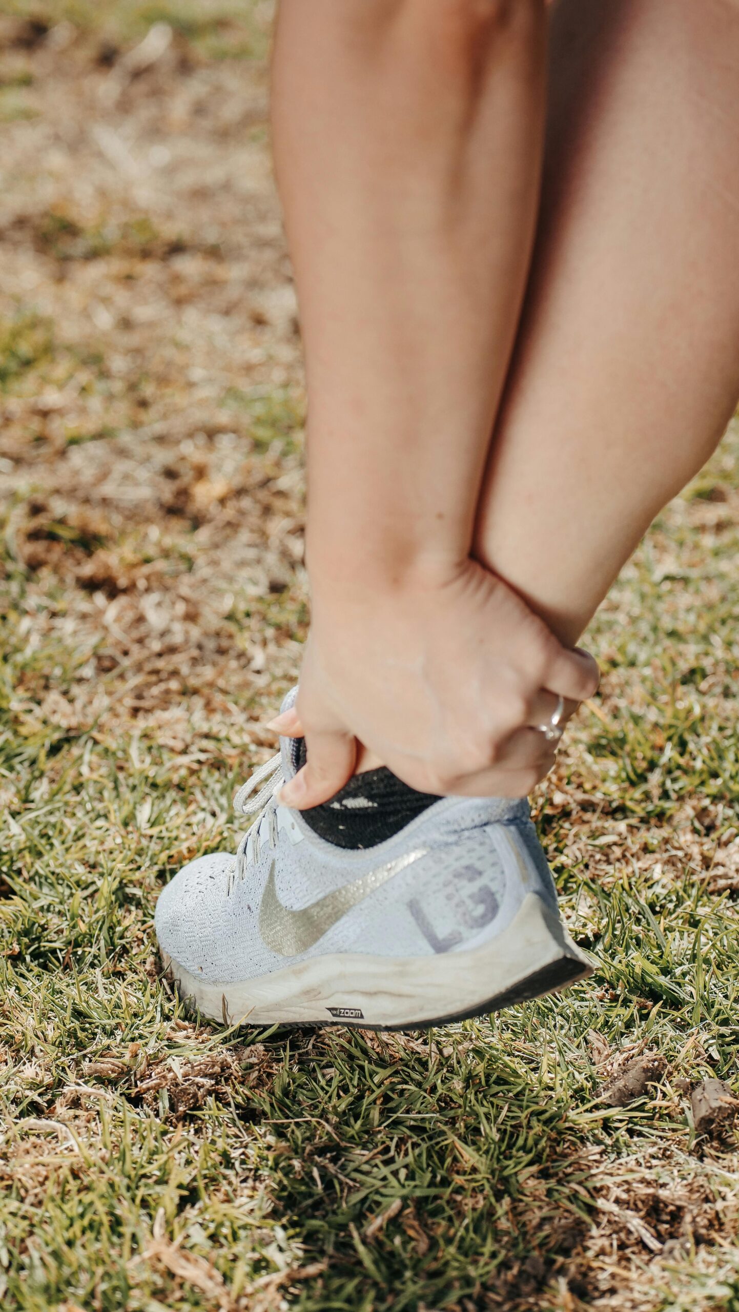 Close-up of a person holding their ankle in a sneaker, indicating pain or injury.
